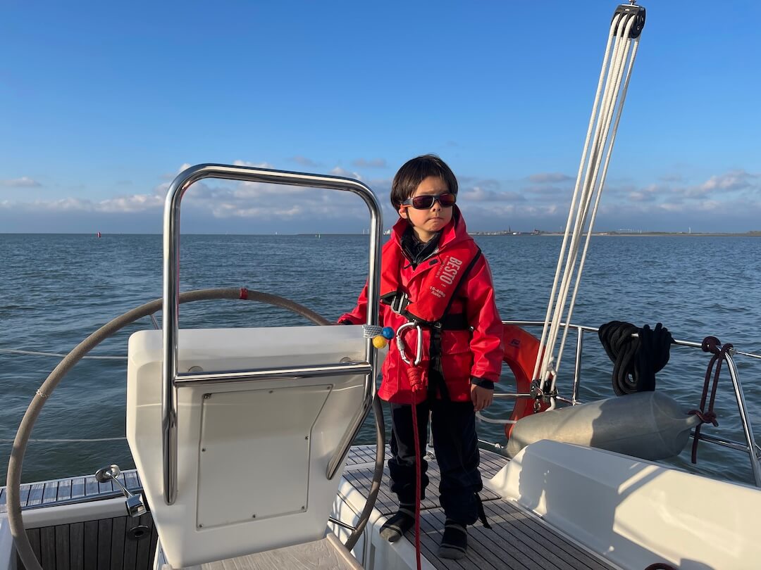 A young crew member standing at the helm of a sailboat underway